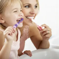 Mama i córka myją zęby. Zapobiegają niemyte zęby u dzieci, ucząc je higieny.