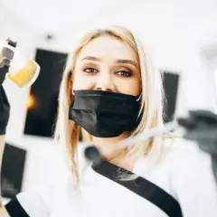 Dentystka w masce przygotowuje się do lakierowania zębów. To zabieg ochronny dla szkliwa.