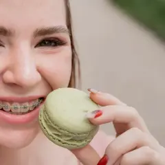 Uśmiechnięta dziewczyna z aparatem ortodontycznym je zielonego makaronika. To dowód, że kiedy można normalnie jeść po założeniu aparatu, życie jest słodsze!