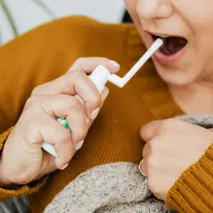 Kobieta aplikuje spray do gardła, szukając ulgi na afty w gardle.