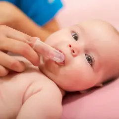 Delikatne czyszczenie ząbków niemowlaka specjalną nakładką na palec. Pokazano, jak myć zęby niemowlakowi.