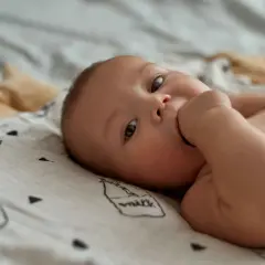 Słodkie niemowlę ssie kciuk przez sen, leżąc na miękkim kocyku z rysunkami.