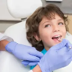 Chłopiec u dentysty, kiedy wypadają 4 mleczne zęby. Lekarz bada jego uśmiech.