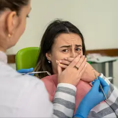 Przerażona pacjentka u dentysty, która żałuje nie mycia zębów na noc. Dentysta w rękawiczkach zbliża się z narzędziami.