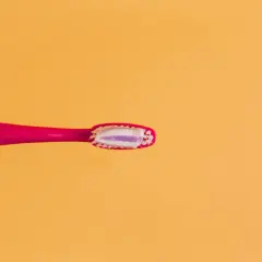 Różowa szczoteczka z biało-fioletową pastą do zębów, zawierającą **fluorek sodu**, gotowa do porannego mycia.