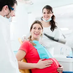 Uśmiechnięta ciężarna pacjentka u dentysty. Dba o zdrowie zębów, by uniknąć próchnicy w ciąży.