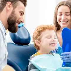 Uśmiechnięty chłopiec po fluoryzacji zębów ogląda swoje zdrowe ząbki w lusterku w kształcie zęba, zadowolony z wizyty u dentysty.