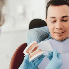 Dentysta pokazuje pacjentowi model szczęki z aparatem ortodontycznym, omawiając, czy trzeba usuwać ósemki do aparatu ortodontycznego.