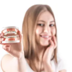 Uśmiechnięta dziewczyna prezentuje model szczęki z kolorowym pierścieniem w aparacie ortodontycznym.