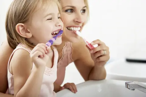 Mama i córka myją zęby. Zapobiegają niemyte zęby u dzieci, ucząc je higieny.