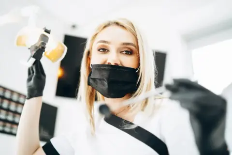 Dentystka w masce przygotowuje się do lakierowania zębów. To zabieg ochronny dla szkliwa.