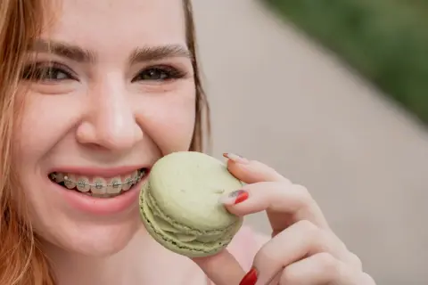 Uśmiechnięta dziewczyna z aparatem ortodontycznym je zielonego makaronika. To dowód, że kiedy można normalnie jeść po założeniu aparatu, życie jest słodsze!