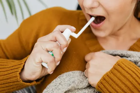 Kobieta aplikuje spray do gardła, szukając ulgi na afty w gardle.