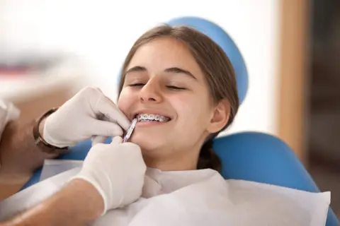 Uśmiechnięta dziewczyna z aparatem ortodontycznym, której dentysta delikatnie czyści zęby.
