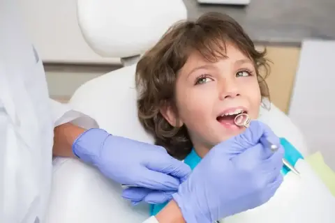 Chłopiec u dentysty, kiedy wypadają 4 mleczne zęby. Lekarz bada jego uśmiech.