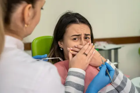 Przerażona pacjentka u dentysty, która żałuje nie mycia zębów na noc. Dentysta w rękawiczkach zbliża się z narzędziami.