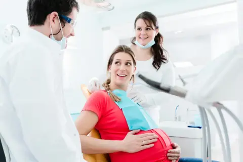 Uśmiechnięta ciężarna pacjentka u dentysty. Dba o zdrowie zębów, by uniknąć próchnicy w ciąży.