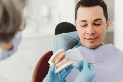 Dentysta pokazuje pacjentowi model szczęki z aparatem ortodontycznym, omawiając, czy trzeba usuwać ósemki do aparatu ortodontycznego.