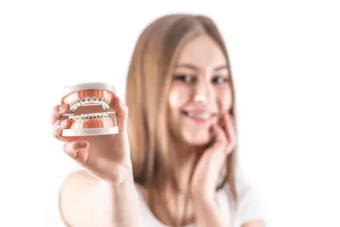 Uśmiechnięta dziewczyna prezentuje model szczęki z kolorowym pierścieniem w aparacie ortodontycznym.