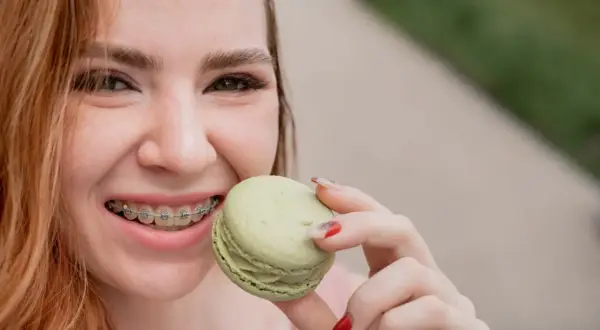 Uśmiechnięta dziewczyna z aparatem ortodontycznym je zielonego makaronika. To dowód, że kiedy można normalnie jeść po założeniu aparatu, życie jest słodsze!