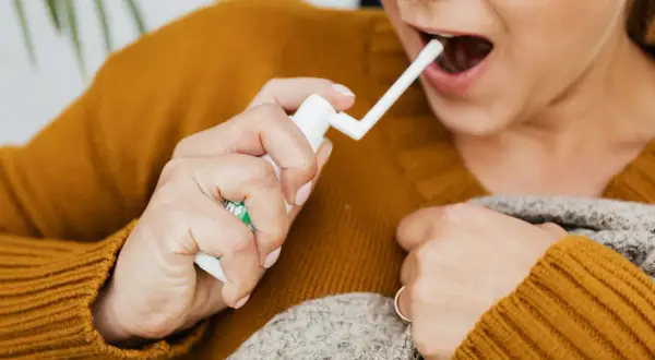 Kobieta aplikuje spray do gardła, szukając ulgi na afty w gardle.