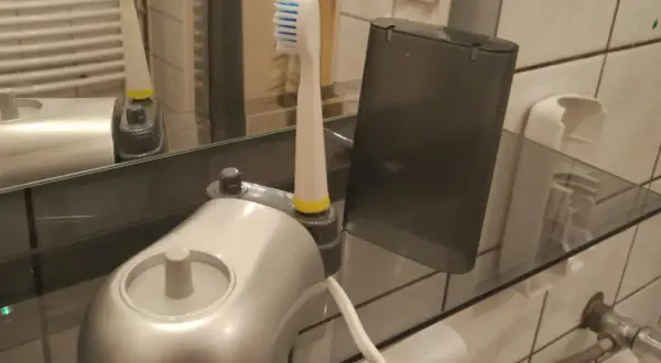 Elektroniczna szczoteczka do zębów i jej wymienna końcówka stoją na szklanej półce, pokazując, jak przechowywać szczoteczki do zębów w łazience.