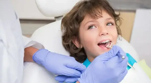 Chłopiec u dentysty, kiedy wypadają 4 mleczne zęby. Lekarz bada jego uśmiech.
