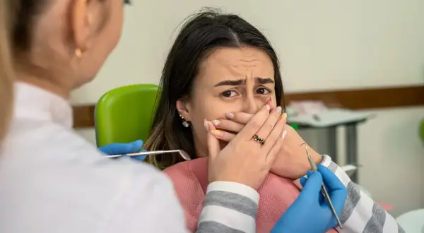 Przerażona pacjentka u dentysty, która żałuje nie mycia zębów na noc. Dentysta w rękawiczkach zbliża się z narzędziami.