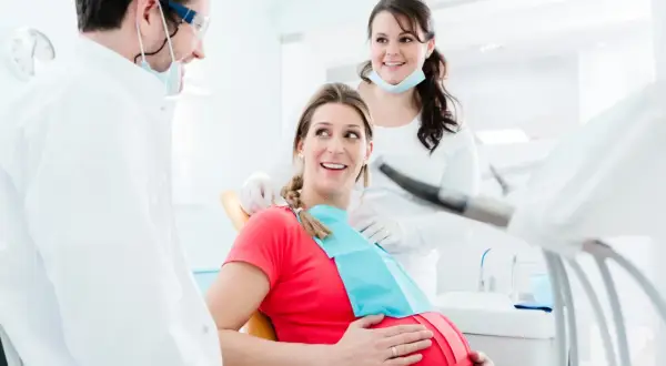 Uśmiechnięta ciężarna pacjentka u dentysty. Dba o zdrowie zębów, by uniknąć próchnicy w ciąży.