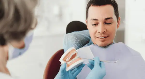 Dentysta pokazuje pacjentowi model szczęki z aparatem ortodontycznym, omawiając, czy trzeba usuwać ósemki do aparatu ortodontycznego.