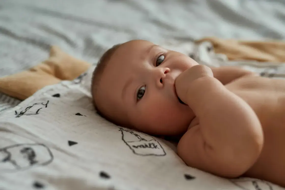 Słodkie niemowlę ssie kciuk przez sen, leżąc na miękkim kocyku z rysunkami.