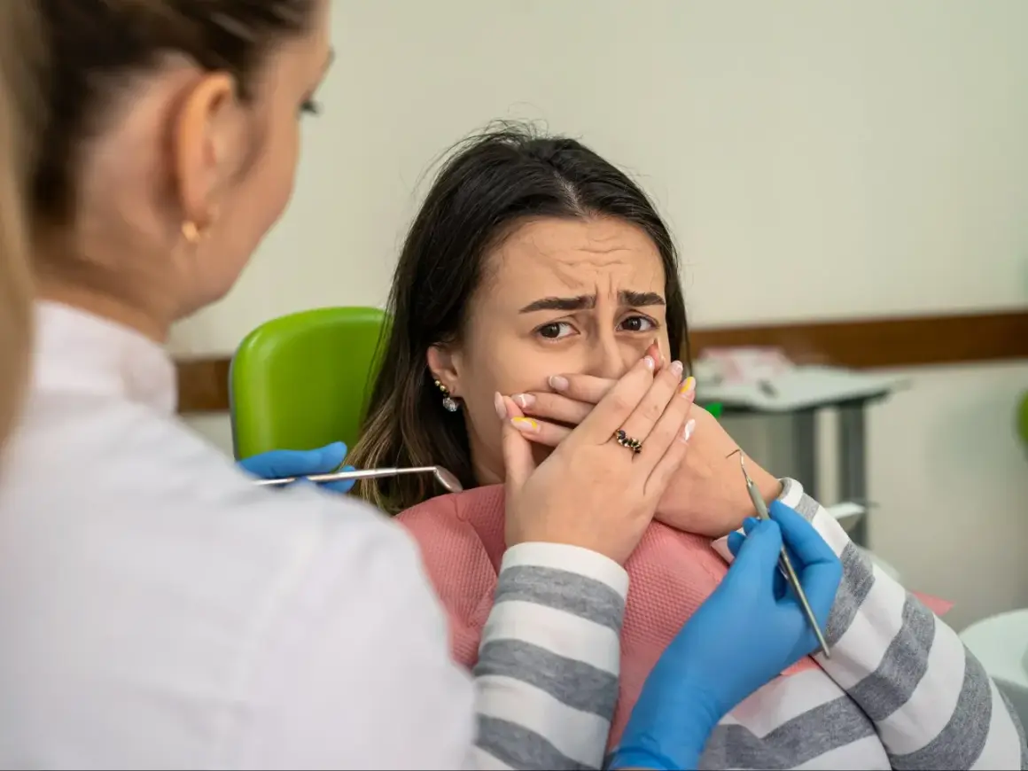 Przerażona pacjentka u dentysty, która żałuje nie mycia zębów na noc. Dentysta w rękawiczkach zbliża się z narzędziami.