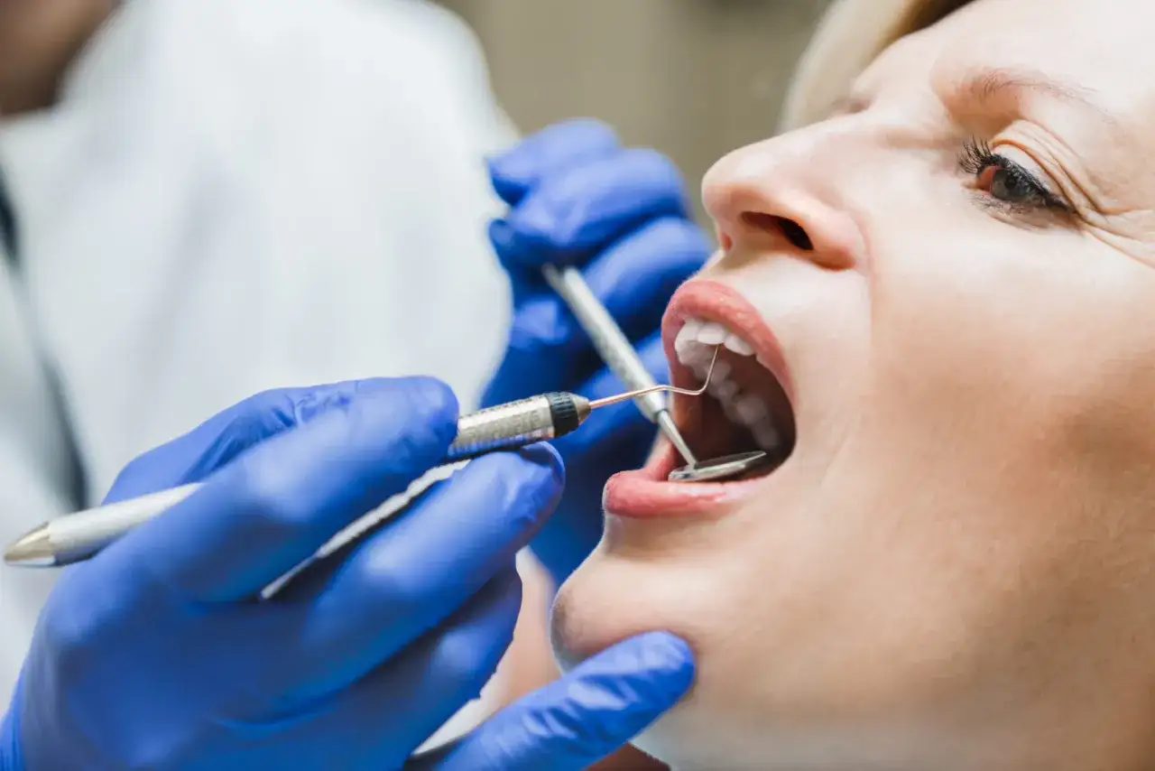Dentysta bada ząb, kt&oacute;ry reaguje na ciepło. Widoczne narzędzia stomatologiczne i usta pacjentki.