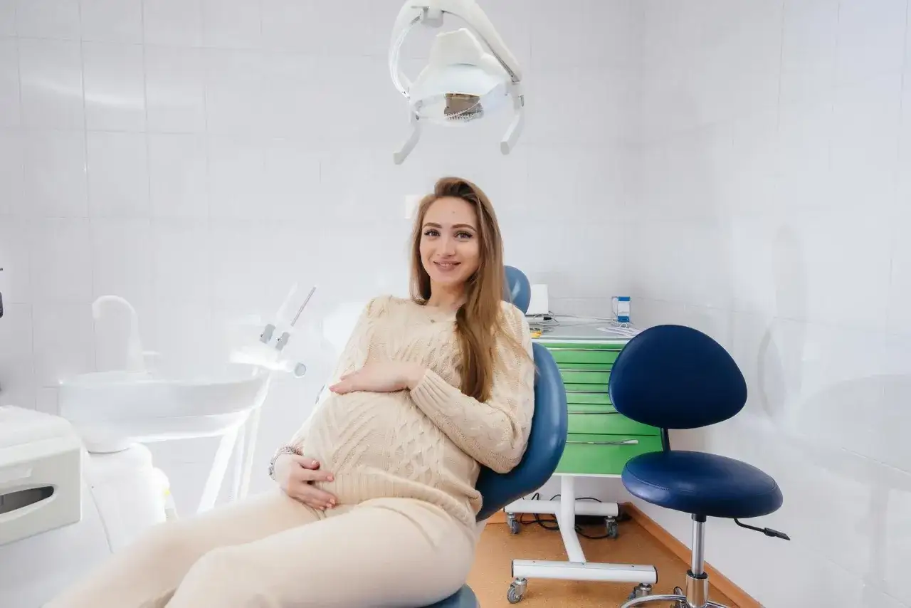 Uśmiechnięta ciężarna kobieta w gabinecie stomatologicznym, dbająca o zdrowie zęb&oacute;w, by uniknąć pr&oacute;chnicy w ciąży.
