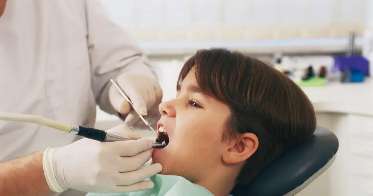 Chłopiec u dentysty. Zabieg lakierowania zęb&oacute;w chroni przed pr&oacute;chnicą.